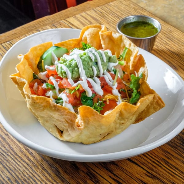 A taco salad in a crispy tortilla bowl, topped with guacamole, sour cream, and salsa.
