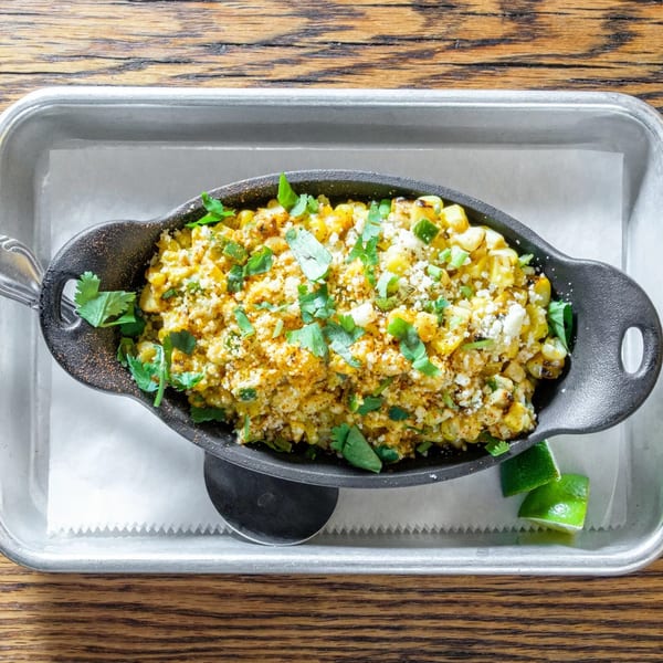 Elote, Mexican street corn, in a black cast iron dish with cilantro and lime wedges.