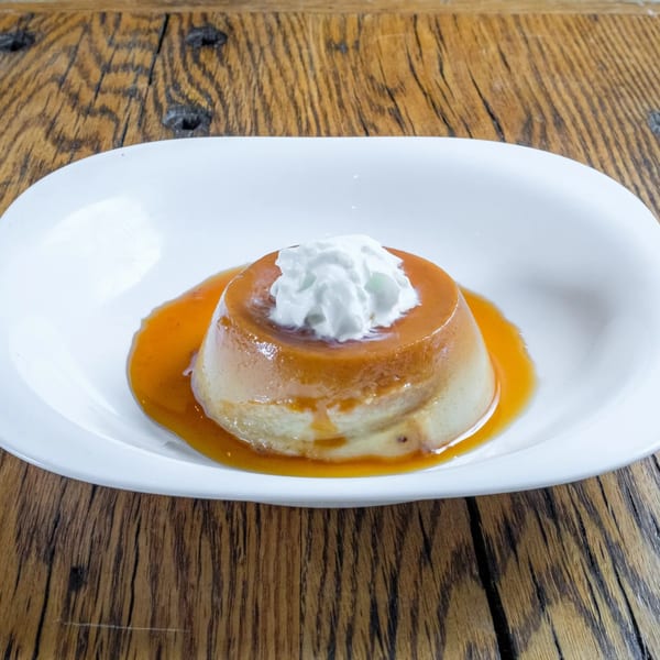 Flan dessert with caramel sauce and whipped cream on a white plate, on a wooden table.