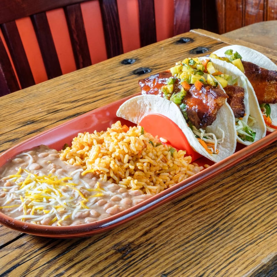 Three tacos with meat and salsa, served with rice and beans on a red platter.