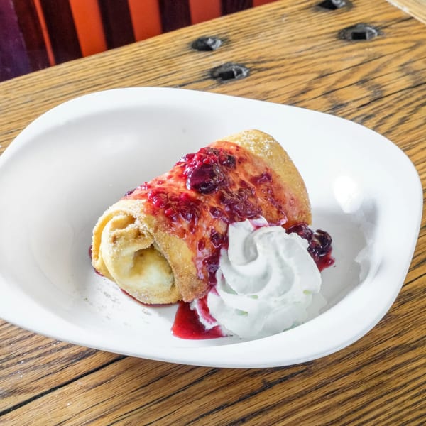 A dessert chimichanga with berry sauce and whipped cream on a white plate at Tortilla Press Cantina.