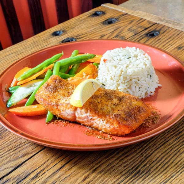 Spiced salmon with a lemon wedge, white rice, green beans, and carrots on a red plate.