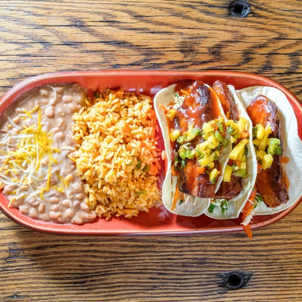 Three fish tacos with mango salsa, rice, and refried beans on a red plate.