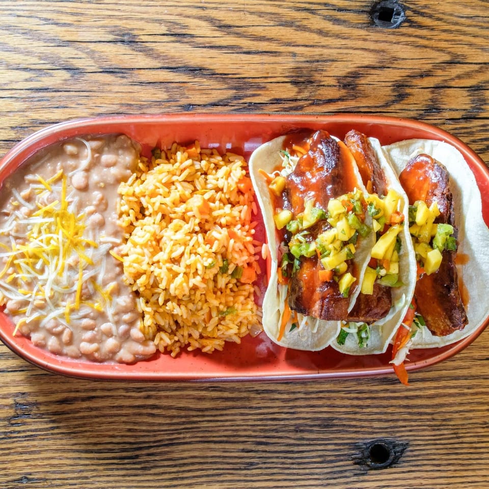 Three fish tacos with mango salsa, rice, and refried beans on a red plate.