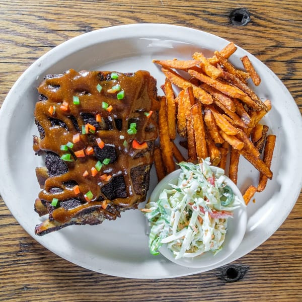 Tortilla Press Cantina's BBQ ribs with sweet potato fries and coleslaw on a white plate.
